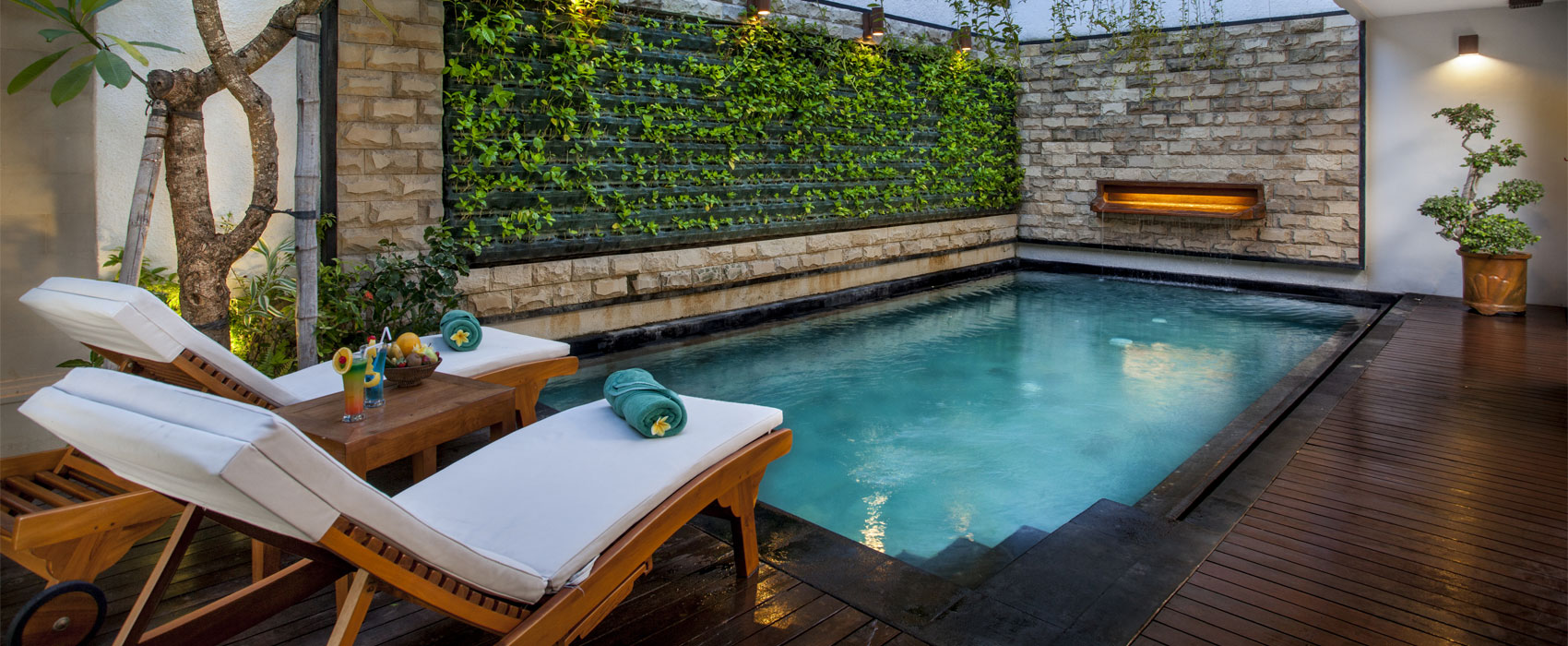 Private plunge pool at Astagina Resort with wooden sun loungers and a vertical garden.