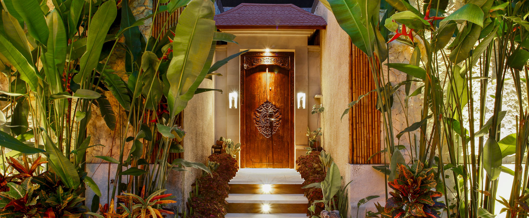 Elegant villa entrance with warm lighting and lush tropical plants at Astagina Resort