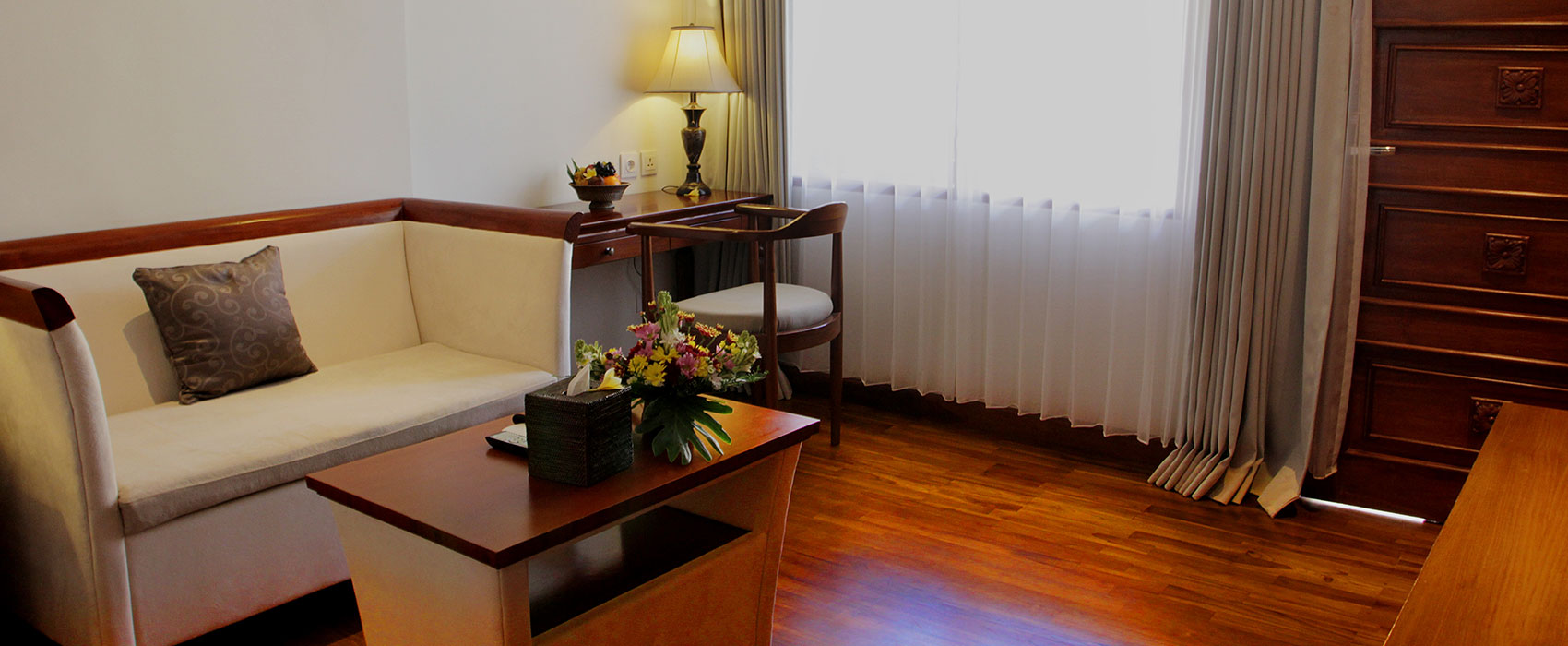 Elegant living room of a Suite Room at Astagina Resort featuring a cream sofa and warm wooden floors.