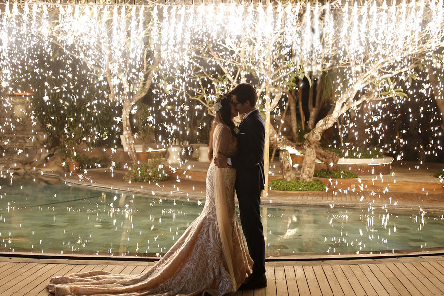 Newlyweds sharing a romantic kiss under a waterfall of golden wedding sparklers.