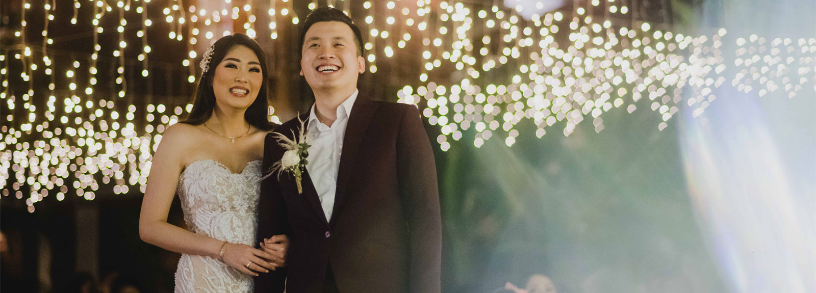 Happy bride and groom smiling under fairy lights at their Astagina Resort wedding reception.