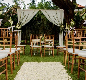 Outdoor garden wedding setup featuring wooden chairs and a white fabric altar at Astagina Resort.