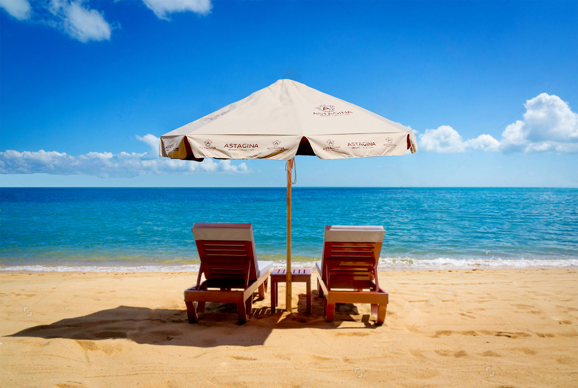 Beach area at Astagina Resort Bali, featuring luxury sun loungers and branded umbrellas with a view of the Ocean