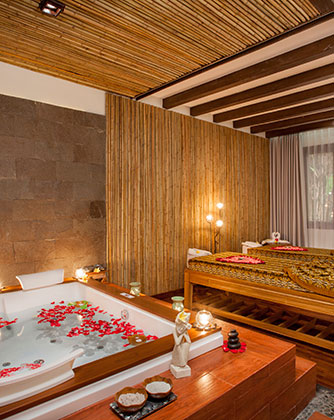 Luxury spa suite at Astagina Resort with a flower-filled bathtub and massage beds.