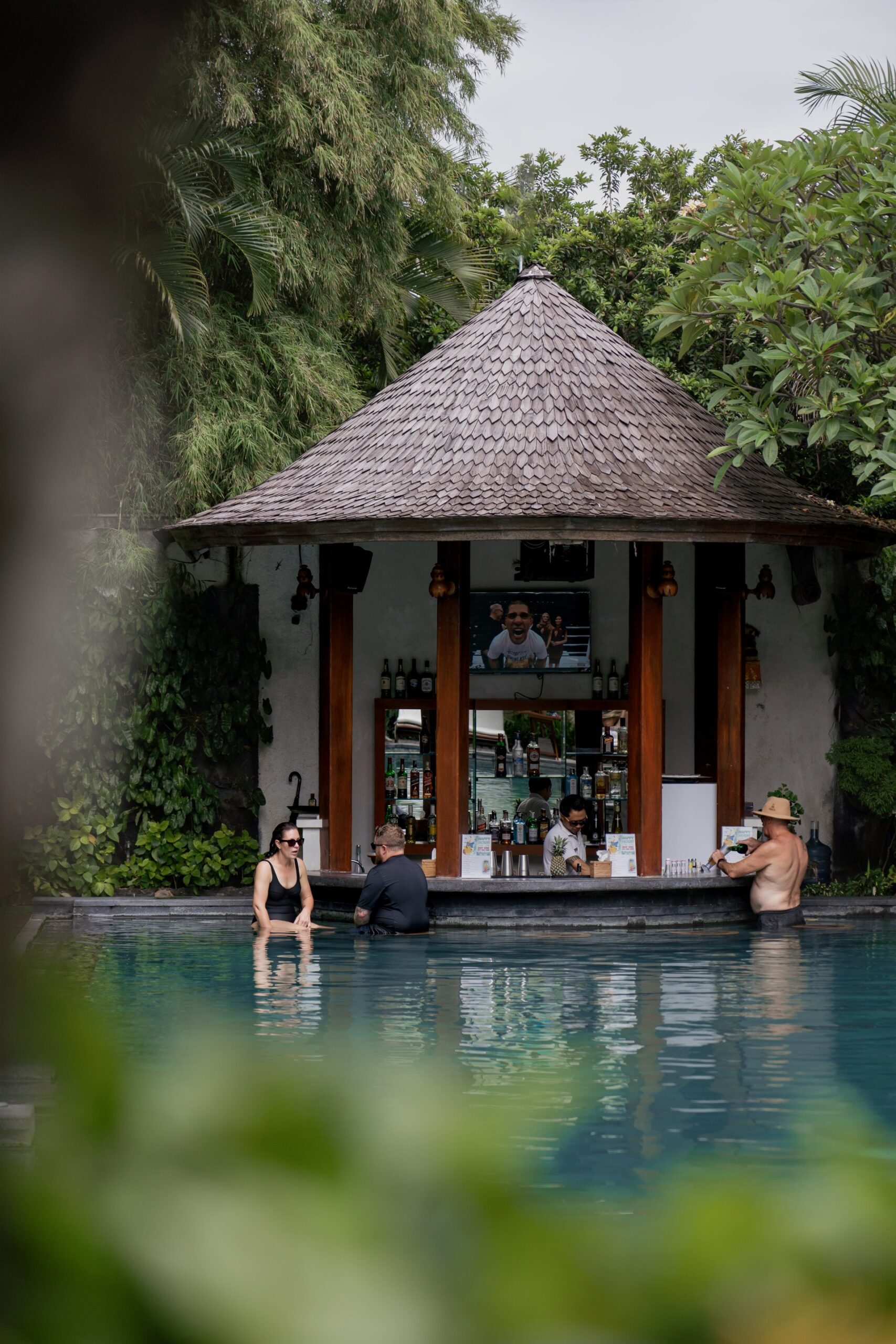 Family at Swim-up pool bar at Astagina Resort surrounded by tropical greenery in Bali.