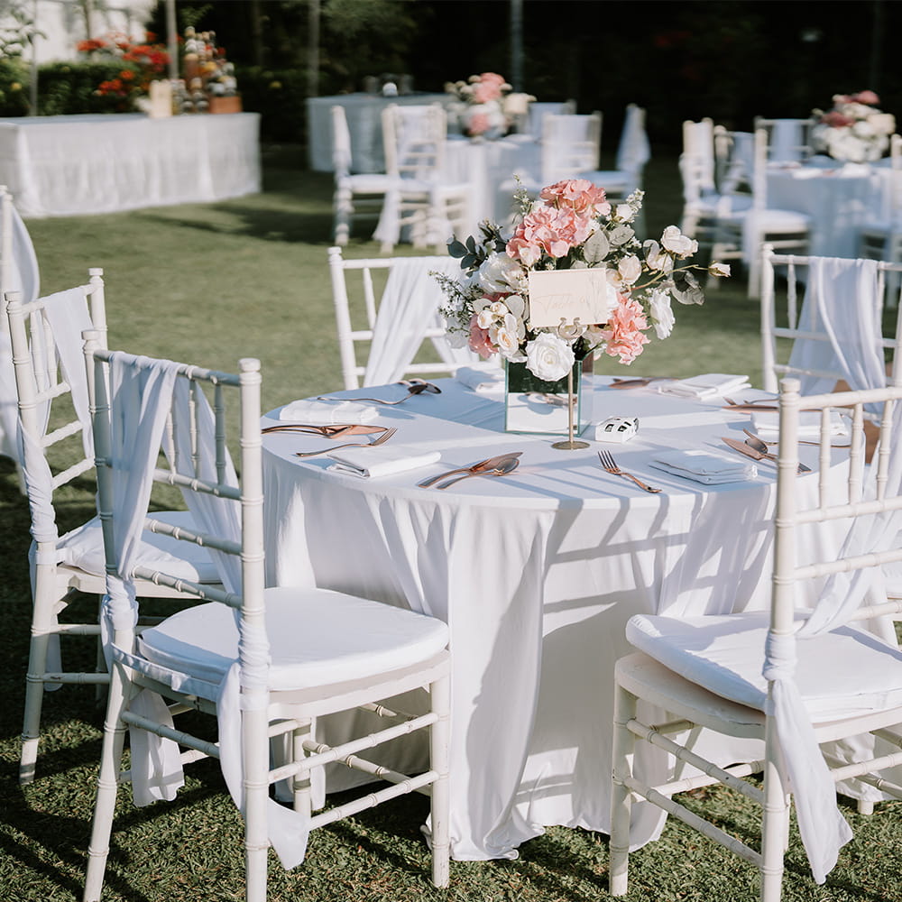 Outdoor wedding reception decorations with round tables, white chairs, and pink and white flower arrangements