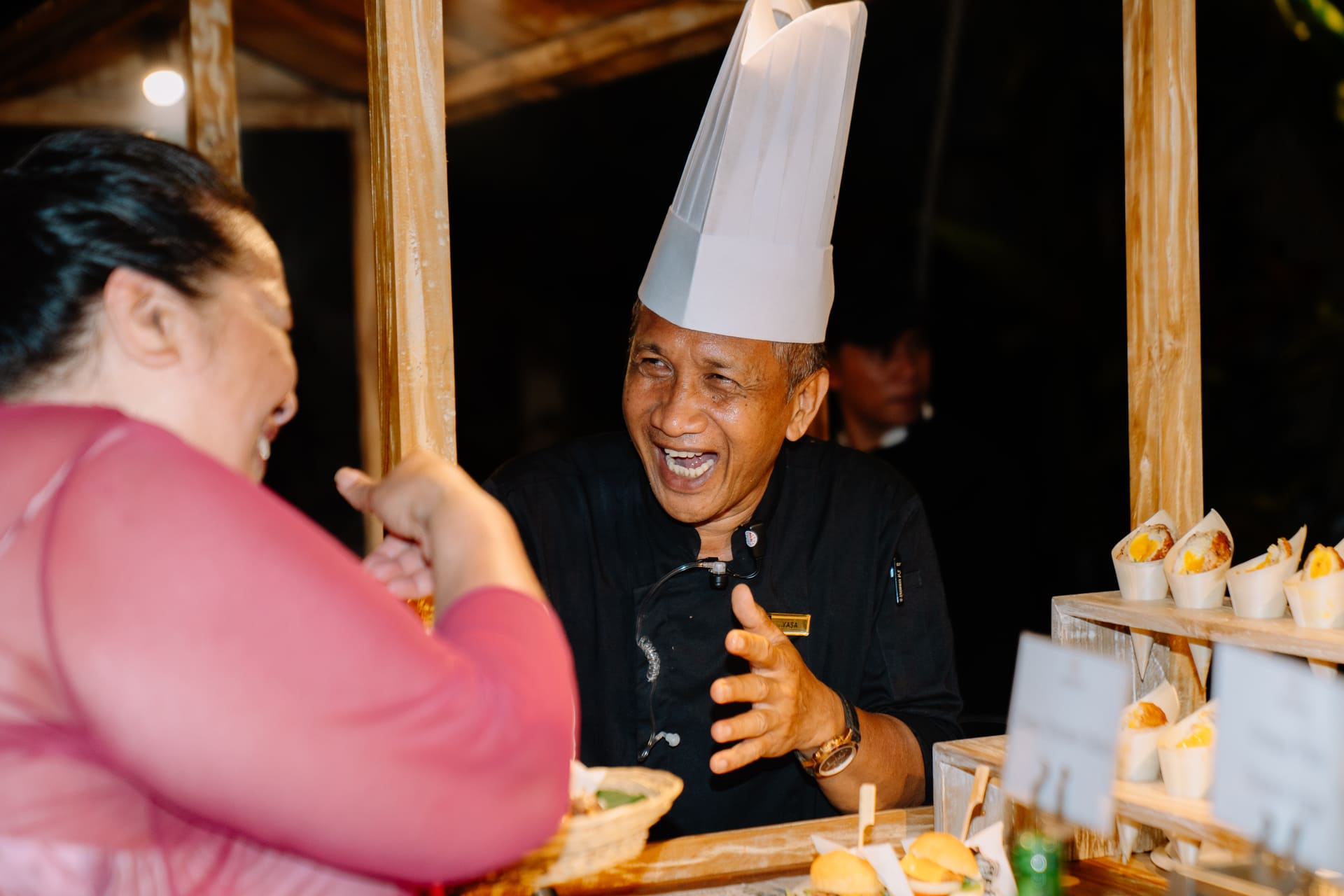 Astagina Resort chef warmly engaging with a guest at a food station during an outdoor event in Legian Bali