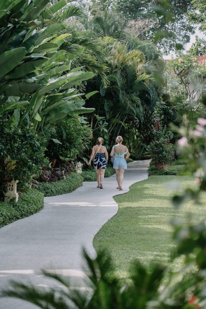 Two Guests walking through the lush tropical gardens of Astagina Resort, finishing a memorable long-term stay near Legian Beach.