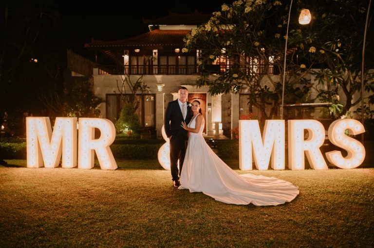 Couple posing in front of illuminated Mr and Mrs marquee letters at night in the garden of Astagina Resort Bali garden wedding venue Legian
