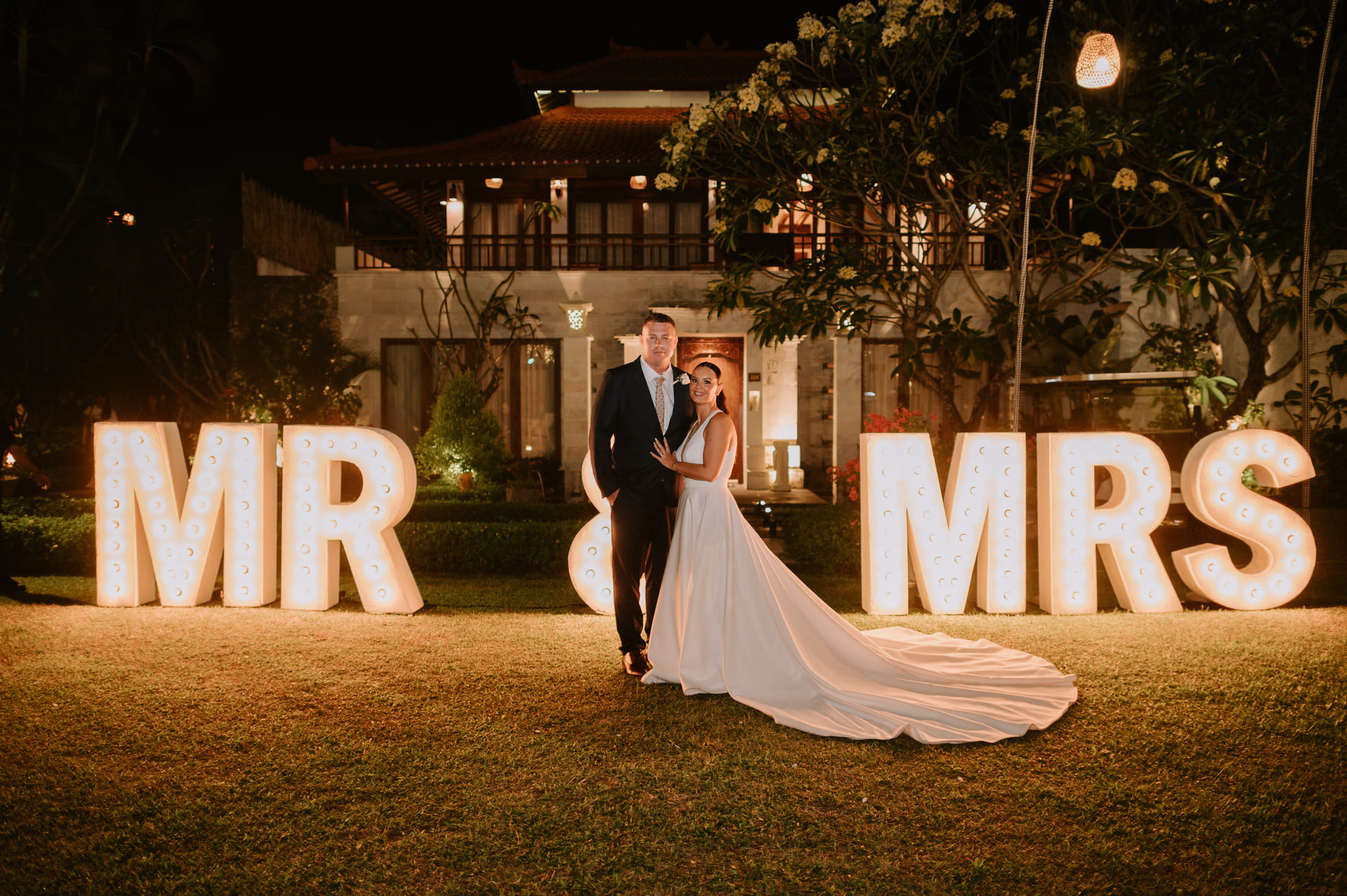 Couple posing in front of illuminated Mr and Mrs marquee letters at night in the garden of Astagina Resort Bali garden wedding venue Legian