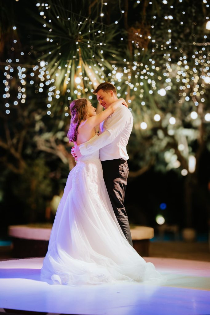 Couple sharing first dance under hanging fairy lights in tropical garden at night during wedding reception at Astagina Resort Bali garden wedding venue