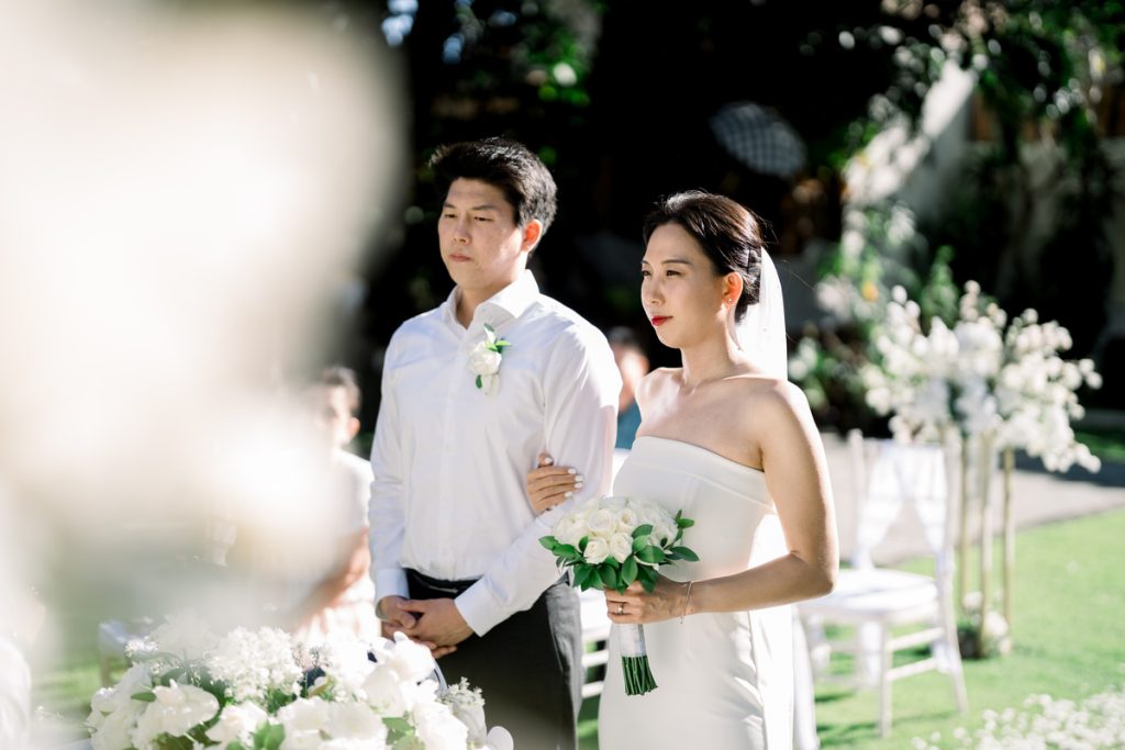 Elopement wedding couple walking down the garden aisle at Astagina Resort Bali surrounded by white floral arrangements