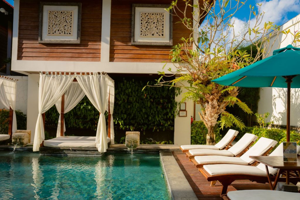 Balinese-style pool area with white canopy daybed and sun loungers surrounded by tropical garden at Astagina Resort Legian Bali