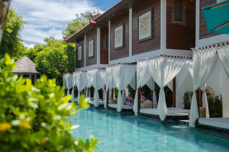 Guests relaxing in poolside cabanas with white drape curtains at Astagina Resort Villa and Spa Legian Bali shoulder season luxury stay